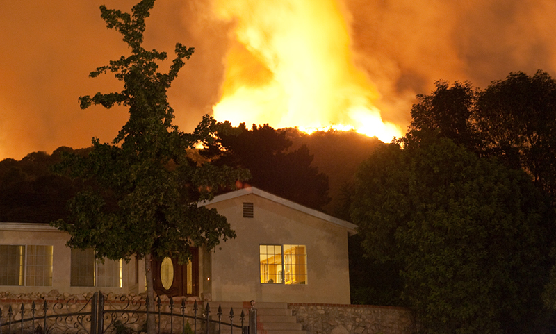 A wildfire creeping up behind a residential home. 